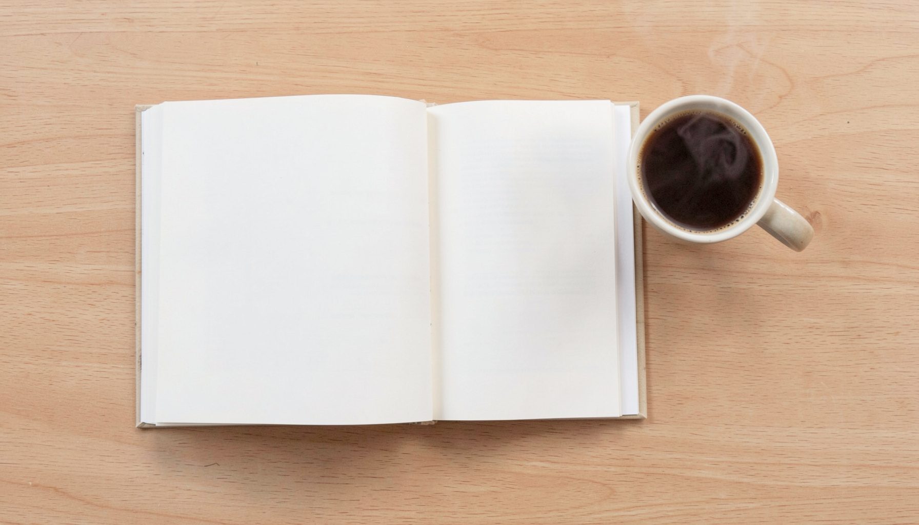 Overhead flat-lay photograph of an open paperback book resting on a light wooden desk next to a steaming cup of coffee, with warm beige and soft brown tones and a calm, focused mood.